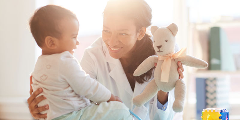 Doctor charms an infant with a teddy bear